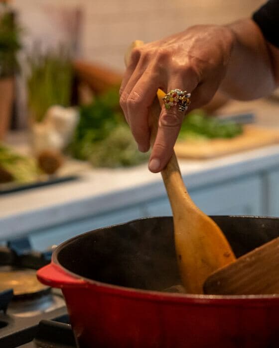 Des mains remuent un plat qui mijote dans une cocotte